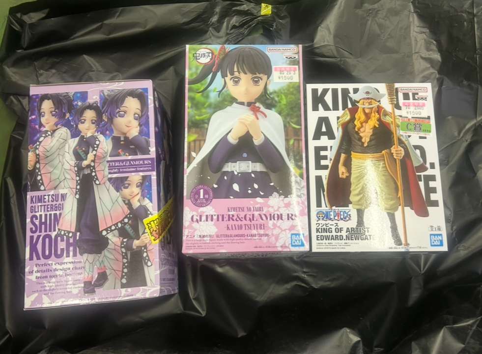 Img_0223 - Articulos Japan (post Box Japan) Three boxed anime figures on a black surface: left a purple Demon Slayer box, middle a pink box with a girl in a cape, right a One Piece Whitebeard figure box. Articulos Japan (Post Box Japan)