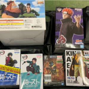 Assorted Japanese anime figure boxes arranged on a black surface, featuring Naruto and Demon Slayer characters.