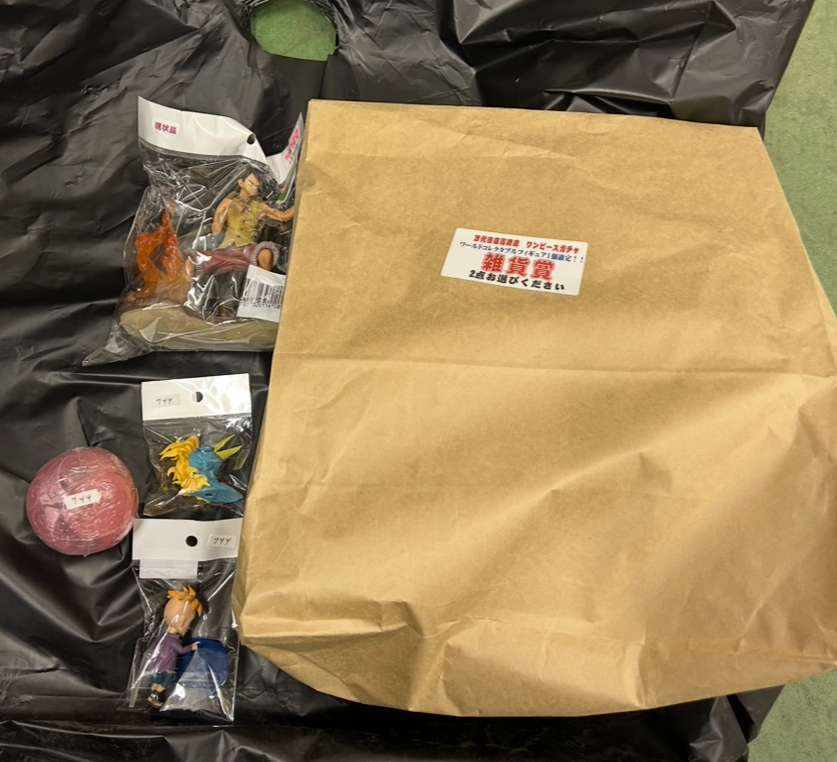 Img_0233 2 - Articulos Japan (post Box Japan) Brown paper bag resting on a black plastic surface, with several small toy figures in clear bags and a pink round ball nearby. Articulos Japan (Post Box Japan)