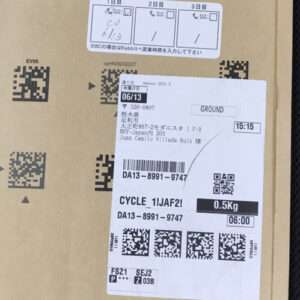 Cardboard box with a white shipping label showing weight 0.5 kg, time 06:00, barcodes/QR codes, and printed tracking details.