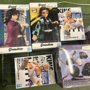 Assorted anime figure boxes on a store shelf, including Grandista Tanjiro figures and other characters with a '20% OFF' sticker visible.