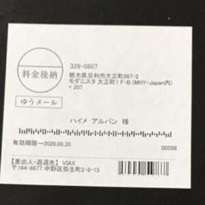 White Japanese mailing label featuring a round seal, a boxed 'ゆうメール' stamp, recipient name, address lines, and a vertical barcode area at the bottom right.