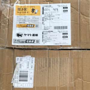 Two brown cardboard boxes stacked; front label shows Japanese shipping info, barcodes, Yamato Transport logo, and a yellow warning sticker.