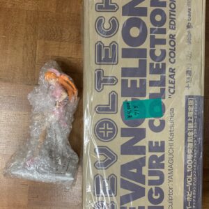 Beige cardboard box with bold blue lettering on a wooden floor, next to a small bubble-wrapped package containing a pink and orange object.