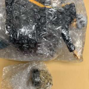 Two bubble-wrapped items on a yellow-brown surface; the larger package contains a dark rectangular object with a visible grip and yellow line.