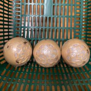 Three round steamed buns with decorative lattice patterns, wrapped in plastic, resting in a green perforated basket.