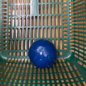 Blue plastic ball resting on the bottom of a green perforated basket with rectangular holes.