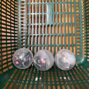 Three small translucent toy capsules in a green perforated basket, each containing a tiny toy inside.
