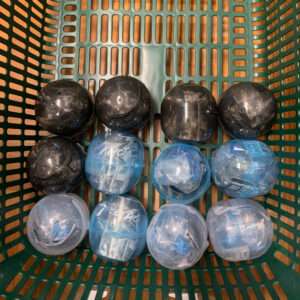 Green shopping basket filled with twelve plastic capsules, black ones on the top row and blue translucent ones below.