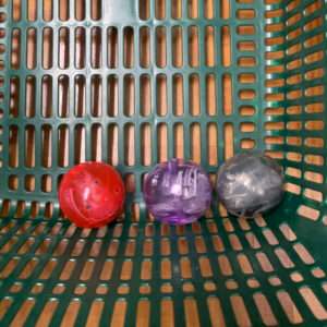Three small plastic capsule toys, red, purple, and gray, resting in a green plastic basket.