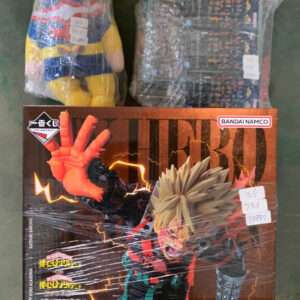 Boxed Bakugo figure from My Hero Academia with lightning effects on a brown box, Bandai Namco logo visible, two wrapped plush toys behind it on a green floor.