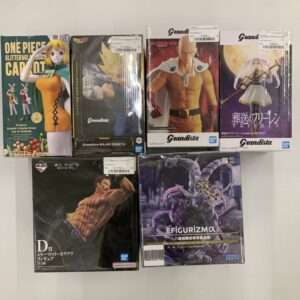 Six boxed anime figurines arranged on a white surface: One Piece figure, Dragon Ball Grandista figure, Saitama figure, purple-haired swordswoman, muscular boxer figure, and SEGA FIGURIZMα dragon statue.