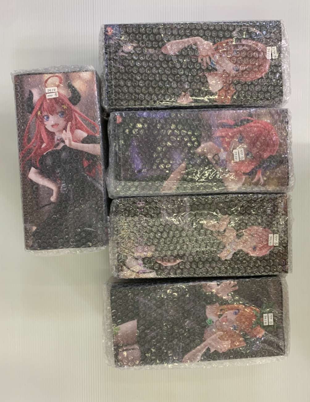 Img_2037 - Articulos Japan (post Box Japan) Stack of five anime figure boxes wrapped in bubble wrap, with a sixth vertical box showing a red-haired girl in a black outfit on the left, all on a light background. Articulos Japan (Post Box Japan)