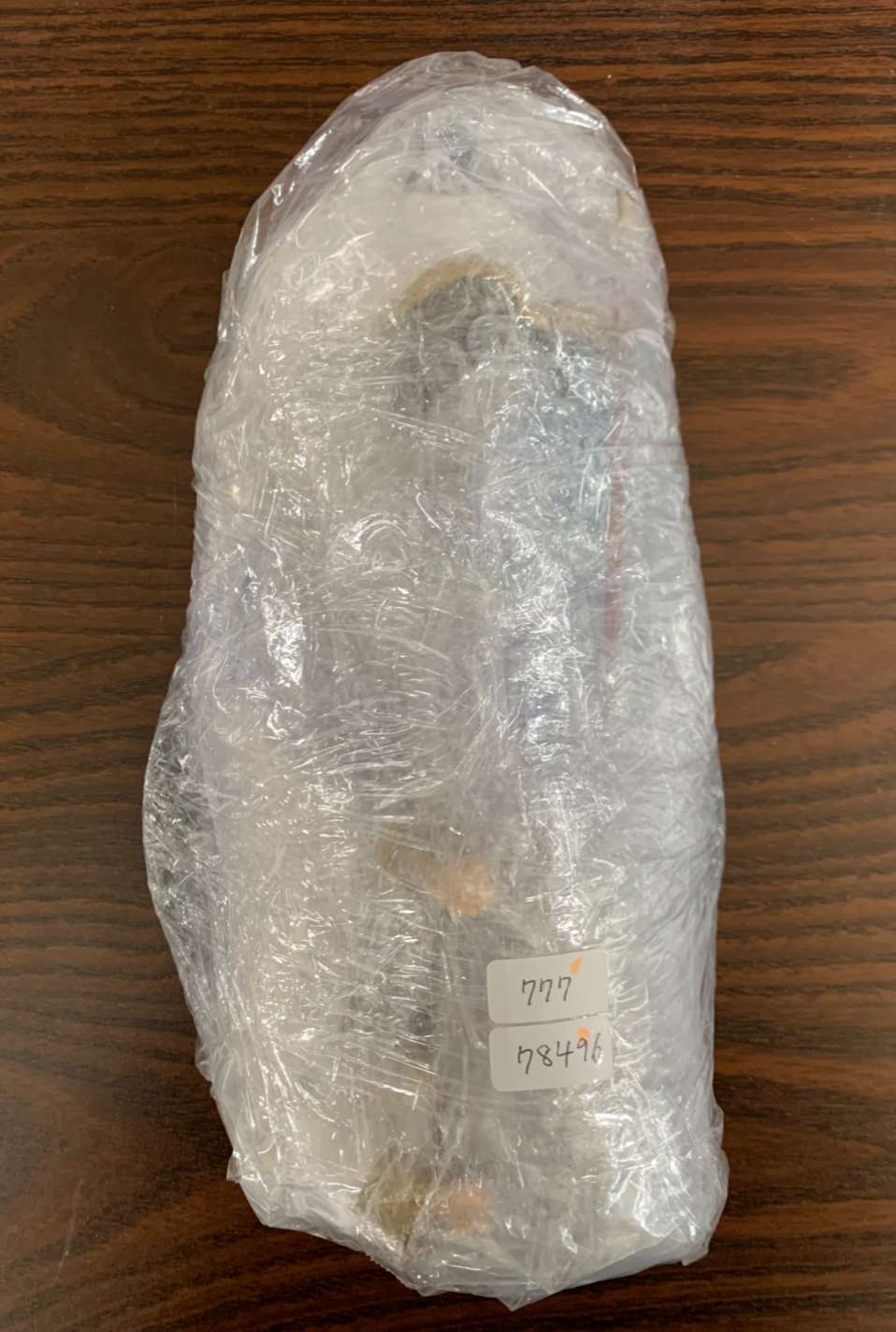 Img_2097 - Articulos Japan (post Box Japan) Tall bottle-like object fully wrapped in clear plastic wrap on a wooden table, with two small sticker labels showing numbers. Articulos Japan (Post Box Japan)