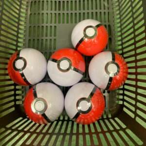 Six red-and-white Poké Balls gathered in a green plastic basket to store or transport them.