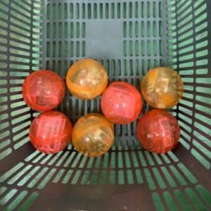 Six small red and orange plastic balls arranged in a green perforated basket.