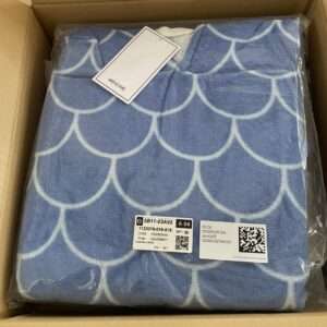 Blue towel in plastic with white scallop/arc pattern inside an open cardboard shipping box