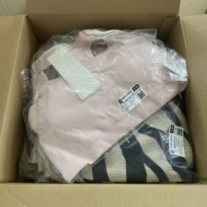 Open cardboard shipping box containing two sealed plastic bags with clothing: a light pink garment and a tan/black zebra-print item with tags attached.