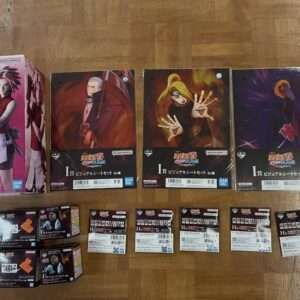 Row of Naruto action figure boxes laid out on a wooden floor, with a pink-clad female box on the left and four large character boxes in the center, plus smaller packs below.