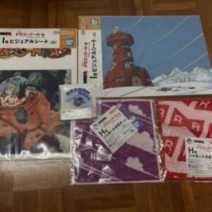 Dragon Ball merchandise laid out on a wooden floor, including poster art, towels, and small 'Dragon Ball' items by Bandai Namco.