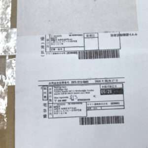 Photo of a Japanese delivery label with postage blocks, addresses, and a barcode on a cardboard box surface, showing shipping details and dates.