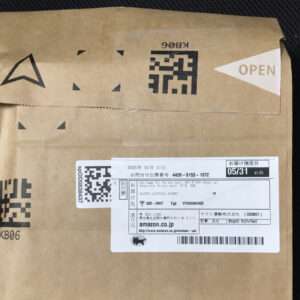 Brown cardboard package with a white shipping label containing a barcode and QR code; small Japanese text and 'amazon.co.jp' visible on the label.