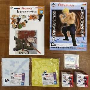 Collection of Dragon Ball merchandise on a wooden floor: boxes, towels, and mini figures from Bandai Namco.  Articulos Japan (Post Box Japan)