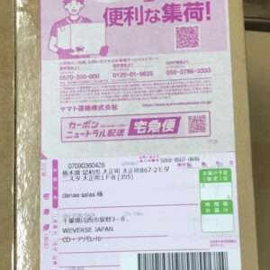 Cardboard box with a large pink shipment label featuring Japanese text, a barcode, and tracking info on the front.