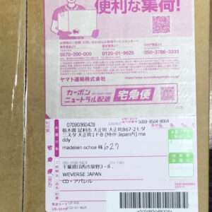Cardboard shipping box with a pink Japanese courier label featuring tracking numbers, recipient address, a barcode, and a QR code.