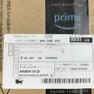 Cardboard box with a white shipping label that contains Japanese text, a barcode, and an Amazon.co.jp reference.