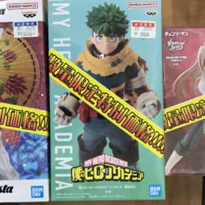 Three Bandai Namco Grandista anime figure boxes on a wooden table, each featuring a different character with a diagonal yellow sale banner across them.
