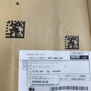 Cardboard box surface with several black QR codes and a white shipping label showing dates and contact info.