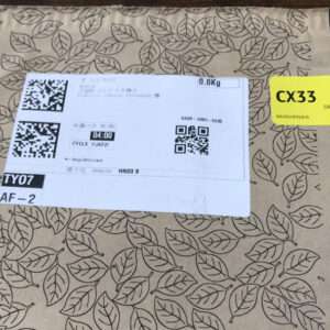Brown cardboard box with a large white shipping label featuring two QR codes and tracking text; a bright yellow CX33 driver tag on the top right.