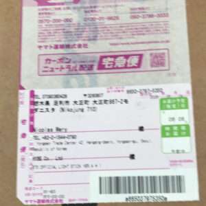 Pink Japanese shipping label on a cardboard box, showing address fields, tracking numbers, and a barcode (Toukyu/宅急便 label).