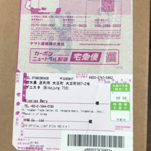 Parcel with pink and white shipping labels on a cardboard box; shows recipient name 'Nicolas Mery', address, barcode, and delivery sticker (Japanese text visible).