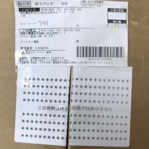 Cardboard parcel with a Japanese shipping label showing a barcode and tracking details, plus a second star-pattern card tied with string to the box.
