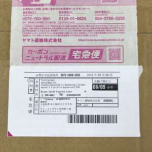 Parcel with Japanese Yamato Transport Takkyubin shipping label: pink and white printed form on a cardboard box, showing a barcode, address fields, and a date stamp.