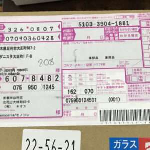 Bright pink Japanese shipping label with tracking numbers, recipient address, and a barcode on a cardboard box.