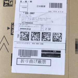 White shipping label on a brown cardboard box featuring Japanese postage text, barcodes, and QR codes; includes 'Do not bend' sign and Amazon listing area.