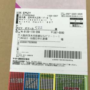 Shipping label on a brown box with a barcode, tracking numbers, and Japanese text; colorful color blocks at the bottom.