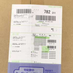 A Japanese shipping label affixed to a brown cardboard box, showing barcodes, tracking numbers, and recipient details.