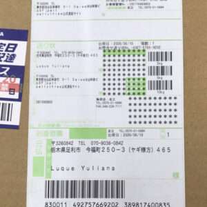 A long Japanese shipping label on brown cardboard, with multiple barcodes, tracking numbers, and recipient details in green and black text.