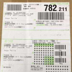 Shipping label on a cardboard box with multiple barcodes, tracking numbers, and recipient/address details in Japanese (package for Vega Perla).