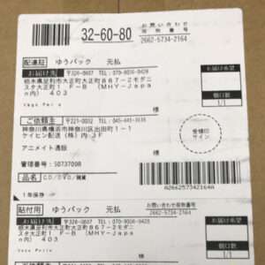 Parcel label on a cardboard box with multiple barcodes, stamps, and sender/recipient addresses in Japanese.