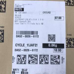 A Japanese shipping label on a cardboard box showing recipient address, service as GROUND, pickup/delivery times, weight 0.8 kg, and multiple barcodes and QR codes.