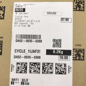 Shipping label on a cardboard box showing destination in Japanese, a barcode, weight 0.2 kg, and QR codes.