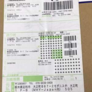 Close-up of a Japanese shipping label on a cardboard box, showing several barcodes, tracking numbers, and green sections.
