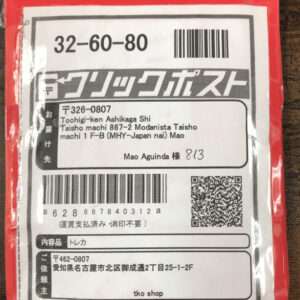 Red package with a white shipping label showing '32-60-80', a barcode, QR code, and Japanese text including the name Mao Aguinda.
