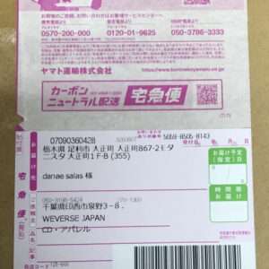 Shipping label on a cardboard box with a pink promotional band at the top, showing sender and recipient details, barcodes, and tracking numbers in Japanese files this parcel info area.