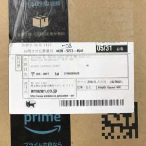 Amazon.co.jp package label on a cardboard box, with a barcode and tracking details visible.